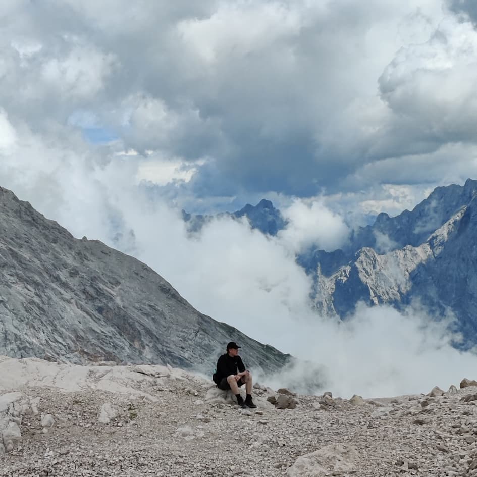 Julian Sibbing sitting on a mountain ridge above the clouds